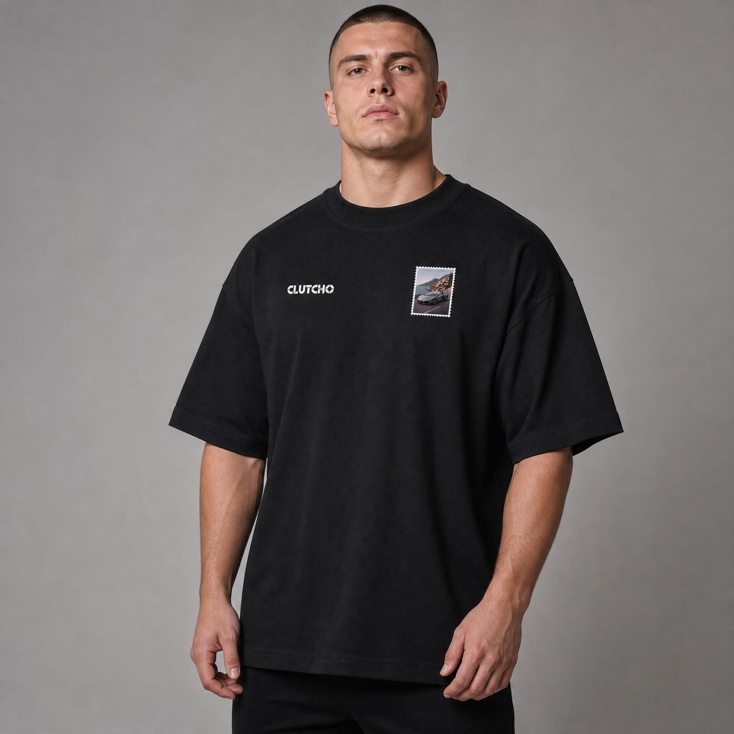 Schwarzes CLUTCHO Amalfi Vibes Oversized T-Shirt Herren, Front-Briefmarke mit italienischem V12-Supersportwagen an der Amalfiküste.