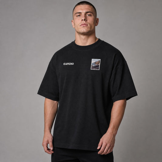 Schwarzes CLUTCHO Amalfi Vibes Oversized T-Shirt Herren, Front-Briefmarke mit italienischem V12-Supersportwagen an der Amalfiküste.
