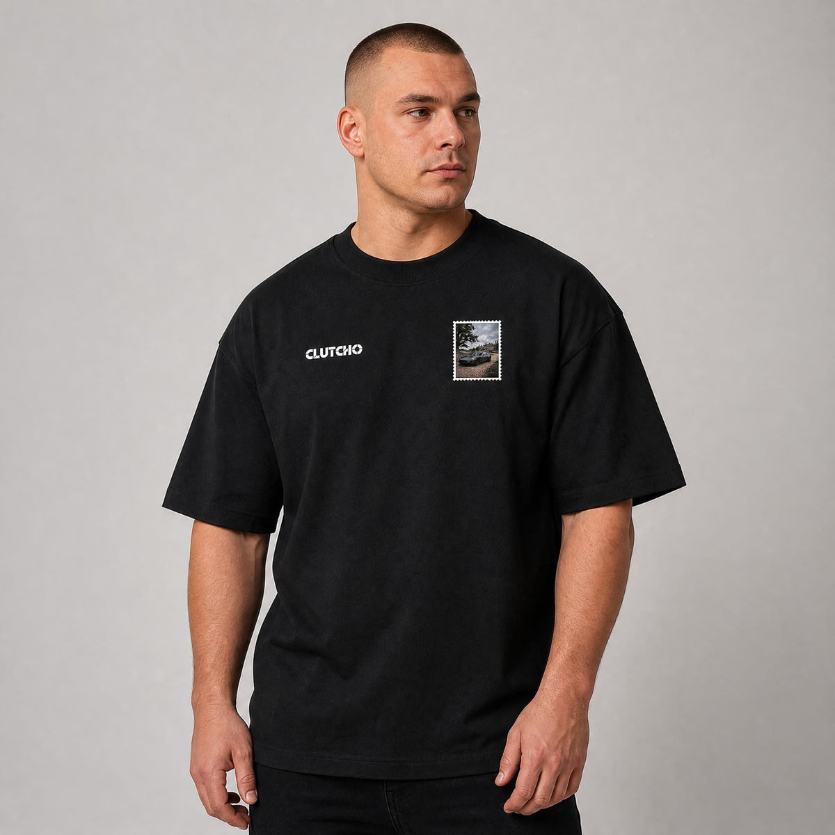Schwarzes CLUTCHO Landgut Oversized T-Shirt Herren, Front-Briefmarke mit britischem Grand Tourer vor einem englischen Landgut.