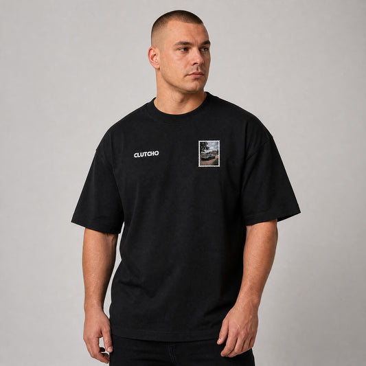 Schwarzes CLUTCHO Landgut Oversized T-Shirt Herren, Front-Briefmarke mit britischem Grand Tourer vor einem englischen Landgut.