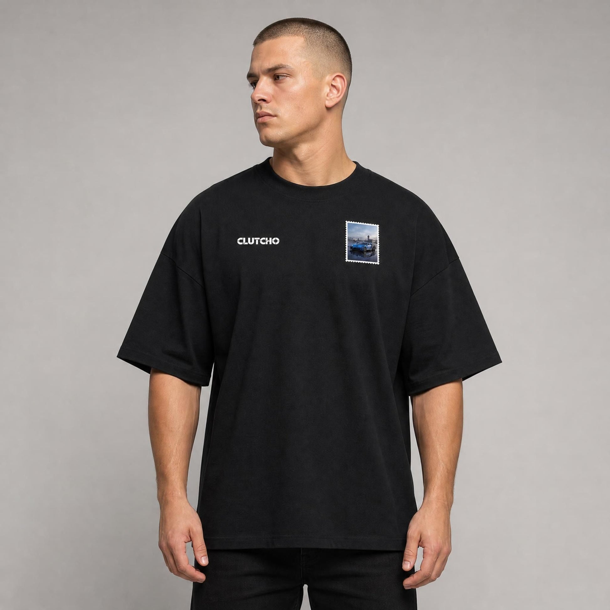 Schwarzes CLUTCHO Jetset Oversized T-Shirt Herren, Front-Briefmarke mit Hypercar auf dem Tarmac eines Privatflughafens.