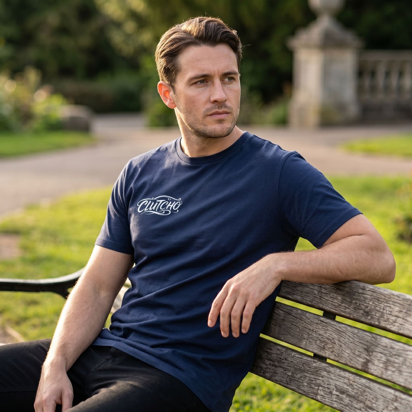 Model seated outdoors wearing the CLUTCHO Tshirt - Shift during golden hour, emphasizing natural fabric flow and fit.