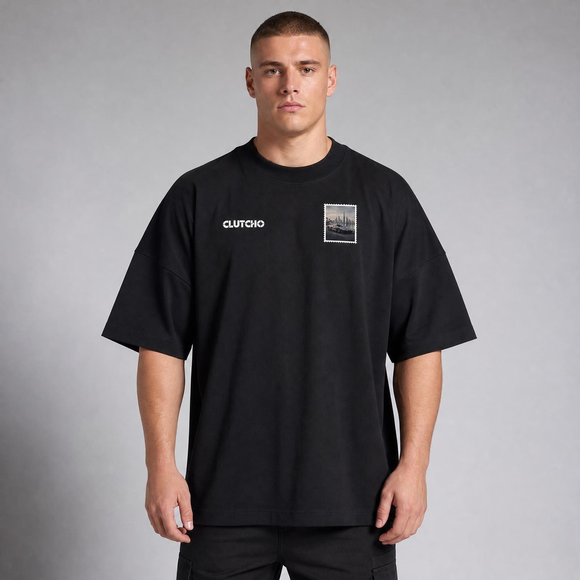 Schwarzes CLUTCHO Dubai Skyline Oversized T-Shirt Herren, Front-Briefmarke mit elektrischem Hypercar vor der Skyline von Dubai.