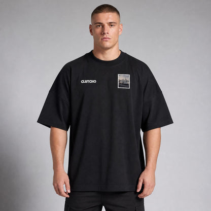 Schwarzes CLUTCHO Dubai Skyline Oversized T-Shirt Herren, Front-Briefmarke mit elektrischem Hypercar vor der Skyline von Dubai.