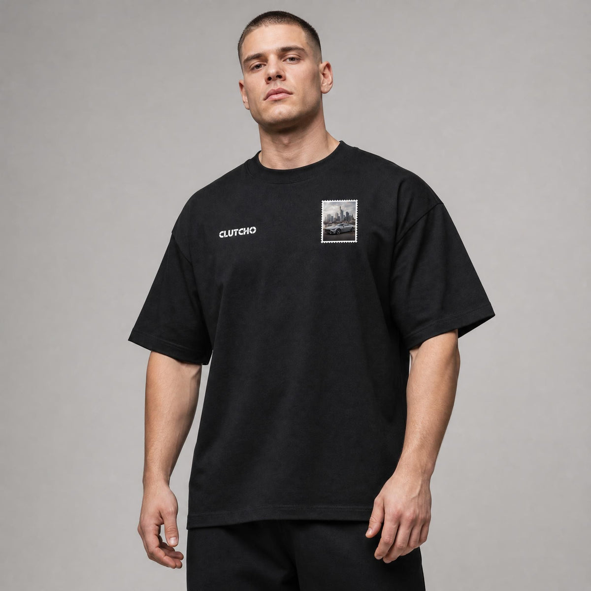 Schwarzes CLUTCHO Frankfurt Skyline Oversized T-Shirt Herren, Front-Briefmarke mit deutschem Sportwagen vor der Frankfurter Skyline.